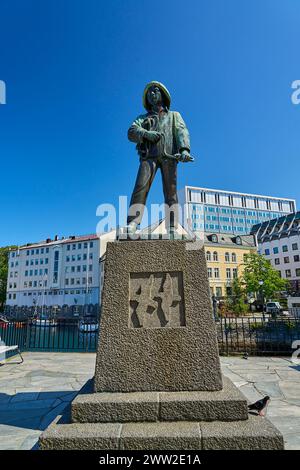 Alesund, Norvegia - 06 07 2022: Statua in bronzo di Skarungen fisher boy nel centro della città di Alesund lungo il porto con case colorate sullo sfondo, Foto Stock