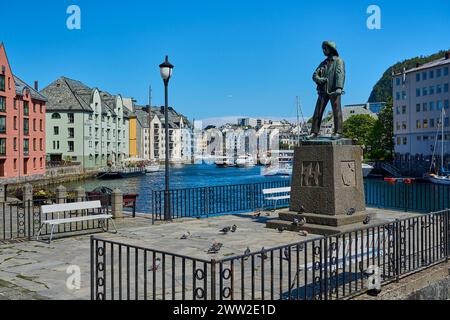 Alesund, Norvegia - 06 07 2022: Statua in bronzo di Skarungen fisher boy nel centro della città di Alesund lungo il porto con case colorate sullo sfondo, Foto Stock