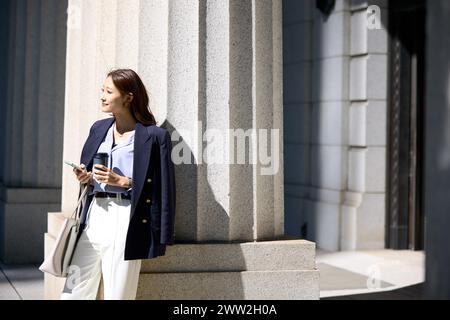 Una donna con un completo e pantaloni bianchi appoggiati a una colonna Foto Stock