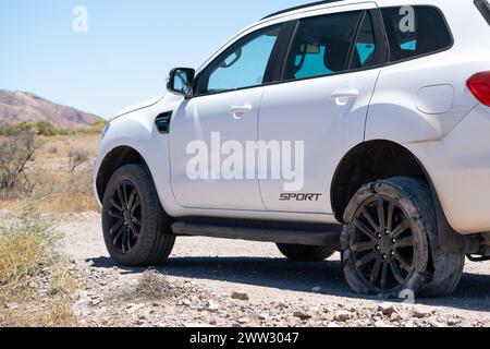 Un SUV laterale con pneumatico sgonfio mette in risalto l'imprevedibilità dei viaggi nell'entroterra. Foto Stock