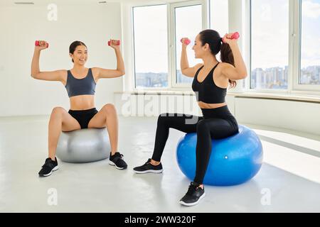 felici e diverse amiche che si allenano con i manubri sulle palle fitness durante la lezione di pilates Foto Stock