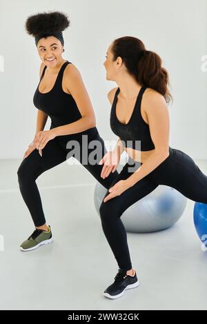 due amiche diverse e felici che si esercitano sulle palle di fitness durante la lezione di pilates, motivazione Foto Stock