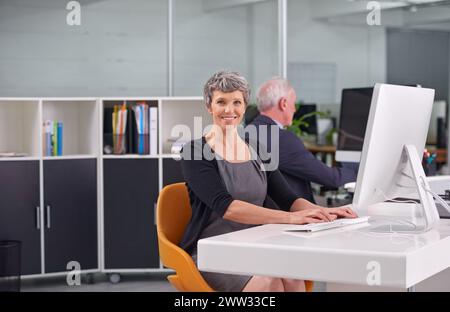 Lavoro, maturo e ritratto di una donna che digita sul pc in ufficio con un collega, un dirigente o un supervisore per l'azienda. Persona Foto Stock