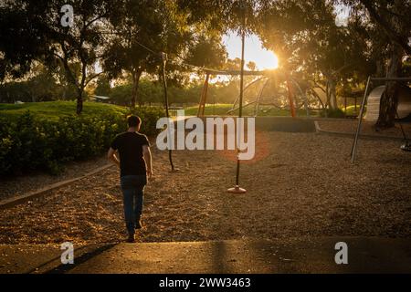 Un uomo cammina verso un sole che tramonta, nel profondo del pensiero, in un parco tranquillo. Foto Stock