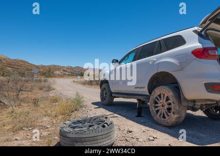 SUV con pneumatico sgonfio su una pista sterrata remota sotto un cielo azzurro. Foto Stock