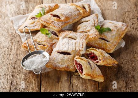 Pasticceria di pasta sfoglia fatta in casa, torte di bacche con zucchero a velo e menta in primo piano sul tavolo. Orizzontale Foto Stock