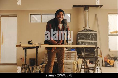 Lavoratore uomo maturo con un sorriso felice, al chiuso in cucina. Sta ristrutturando e migliorando gli interni, concentrandosi su battiscopa e lavorazione del legno. Utilizzando un Foto Stock