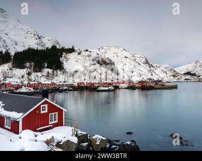 Tradizionali case di rorbu rosse su palafitte nell'autentico villaggio di pescatori di Nusfjord, montagne innevate sullo sfondo, Flakstadoya e Lofoten Foto Stock