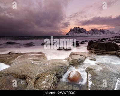 Scogli arrotondati sulla spiaggia di Utakleiv in un'atmosfera suggestiva e nuvolosa, montagne innevate sullo sfondo, isola Vestvagoy, Lofoten, Norvegia Foto Stock