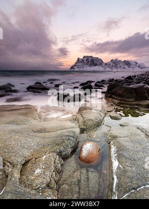 Scogli arrotondati sulla spiaggia di Utakleiv in un'atmosfera suggestiva e nuvolosa, montagne innevate sullo sfondo, isola Vestvagoy, Lofoten, Norvegia Foto Stock