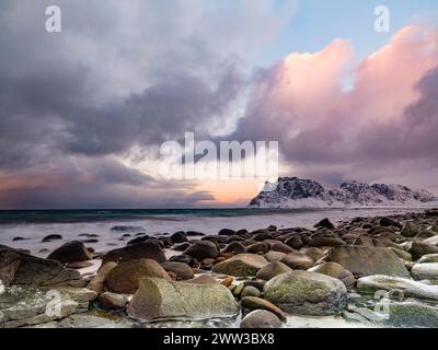 Scogli arrotondati sulla spiaggia di Utakleiv in un'atmosfera suggestiva e nuvolosa, montagne innevate sullo sfondo, isola Vestvagoy, Lofoten, Norvegia Foto Stock