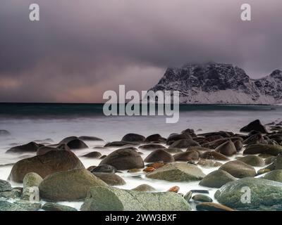 Scogli arrotondati sulla spiaggia di Utakleiv in un'atmosfera suggestiva e nuvolosa, montagne innevate sullo sfondo, isola Vestvagoy, Lofoten, Norvegia Foto Stock