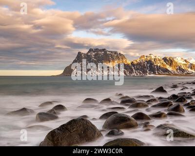 Rocce arrotondate sulla spiaggia di Utakleiv in un'atmosfera spettacolare e nuvolosa, montagne innevate sullo sfondo, Vestvagoya, Lofoten, Norvegia Foto Stock