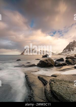 Scogli arrotondati sulla spiaggia di Utakleiv in un'atmosfera suggestiva e nuvolosa, montagne innevate sullo sfondo, isola Vestvagoy, Lofoten, Norvegia Foto Stock