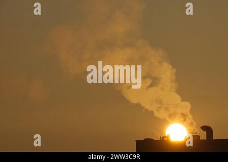 Fumo che fuoriesce dal camino di un edificio multifamiliare sullo sfondo del sorgere del sole, inquinamento atmosferico, riscaldamento degli edifici con gas. Foto Stock