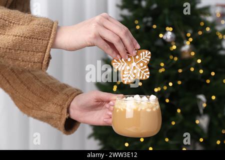 Donna con biscotti decorati e tazza di cacao vicino all'albero di Natale, primo piano Foto Stock