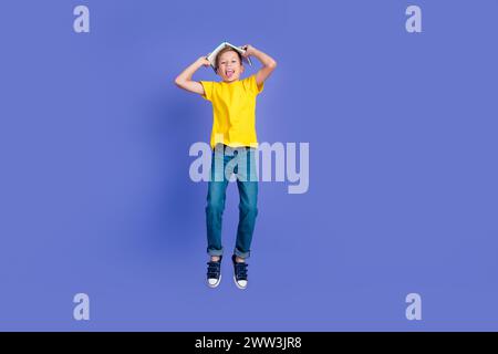 Foto di un ragazzo divertente allegro pazzo che indossa eleganti vestiti gialli salta su divertiti libro sulla testa sfondo isolato di colore viola Foto Stock