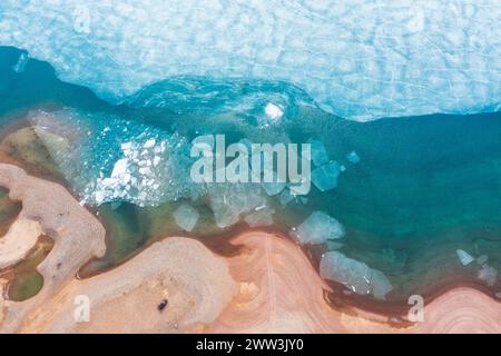 iceberg ghiacciati dall'alto verso il basso, bagnati dall'acqua blu vicino alla spiaggia sabbiosa. Ghiaccio fuso in un lago di montagna. Affascinante armonia di natura incontaminata. GL Foto Stock