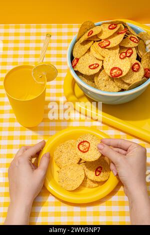 Rotondo di nachos di tortilla di mais con fette di peperoncino rosso in una ciotola con una bevanda fredda Foto Stock