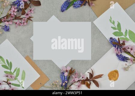 Composizione su un tavolo con piccoli fiori, buste, fogli bianchi e foglie dipinte con spazio vuoto per riempire il contenuto. Foto Stock