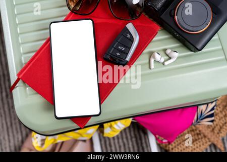 Preparazione per un viaggio, fotocamera smartphone e chiave auto con valigia da viaggio. Foto Stock