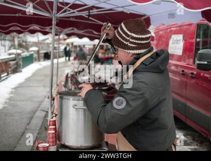 Lanslevillard, Francia, 10 gennaio 2024: Un venditore riempie una tazza di VIN brulé al mercato cittadino Foto Stock