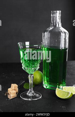 Absinthe, cucchiaio, zucchero di canna e lime sul tavolo nero. Bevanda alcolica Foto Stock