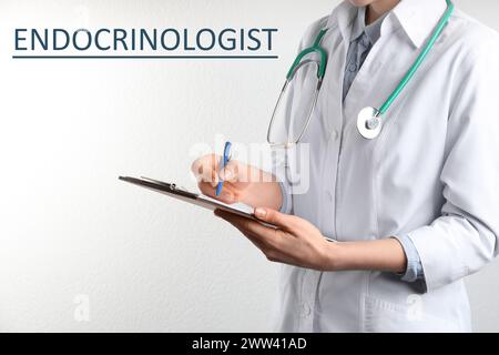 Endocrinologo con stetoscopio, appunti e penna vicino a parete bianca, primo piano Foto Stock