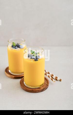 Frullato di mango rinfrescante e sano con scaglie di cocco e mirtilli freschi su sfondo chiaro Foto Stock