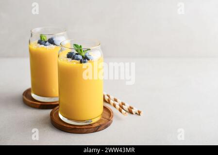 Frullato di mango rinfrescante e sano con scaglie di cocco e mirtilli freschi su sfondo chiaro Foto Stock