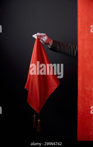 Primo piano che nasconde la mano del mago dietro un tendone rosso che tiene il fazzoletto magico Foto Stock