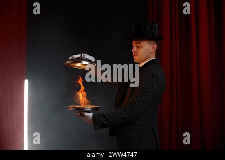 Mago maschile che mostra trucco con illusione di fuoco magico con vassoio in acciaio Foto Stock