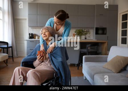 Adorabile figlia adulta che abbraccia la vecchia madre con disabilità seduta in sedia a rotelle Foto Stock