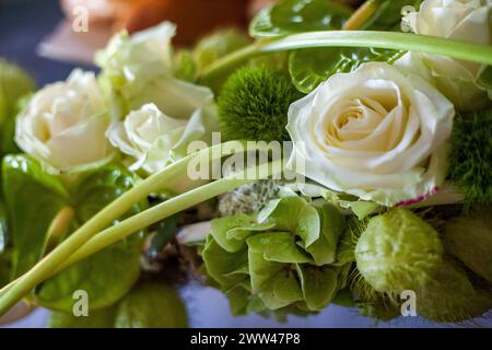 Questa immagine presenta una vista ravvicinata di una composizione floreale con rose bianche incontaminate e un assortimento di vegetazione lussureggiante. Le varie texture e i verdi vibranti creano una freschezza estetica rinfrescante e naturale in Bloom: Delicate rose e lussureggiante vegetazione in un allestimento floreale. Foto di alta qualità Foto Stock