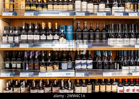 Primo piano su bottiglie di vino allineate su uno scaffale in un negozio, alcol in vendita in negozio di liquori Foto Stock