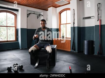 L'uomo con una gamba protesica si siede sulla panca della palestra, guarda un tablet Foto Stock