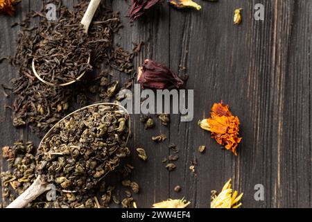 Composizione di tè nero e verde secco in cucchiai vintage, tè fiori secchi su uno sfondo di legno scuro vista dall'alto. Diversi tipi di tè secco Foto Stock