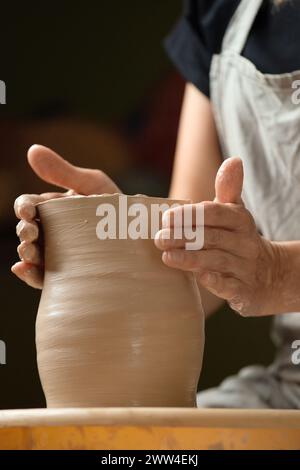 Le mani di una donna lavorano sulla ruota di un vasaio, creando un vaso o una ciotola in ceramica nello studio. Hobby, creatività, ceramica. Prodotto in argilla Foto Stock