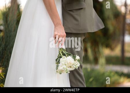 Un paio di sposi novelli nel parco, lo sposo abbraccia la sposa, la sposa regge un bouquet di nozze bianco tra le mani, primo piano Foto Stock