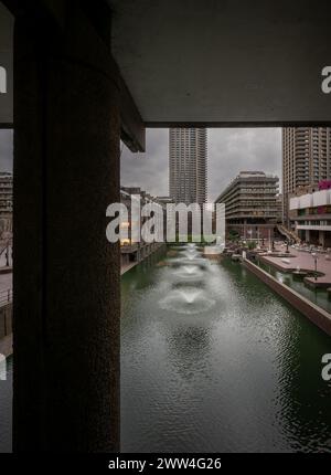 Londra, Regno Unito: Lago artificiale con fontane da una passerella sulla Barbican Estate nella City di Londra. La tenuta Barbican è un esempio importante di Foto Stock
