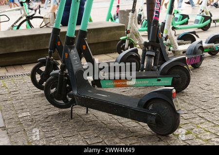 Varsavia, Polonia - 6 agosto 2023: Un gruppo di scooter elettrici parcheggiati disponibili a noleggio, con uno scooter appoggiato su un marciapiede acciottolato. Foto Stock