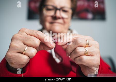 sarta concentrata con occhiali che infilano il filo da cucire nell'ago Foto Stock