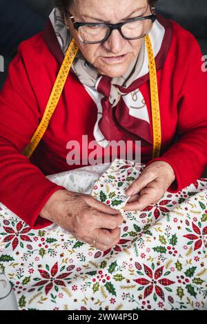 donna anziana sarta che cucisce a mano un indumento di stoffa Foto Stock