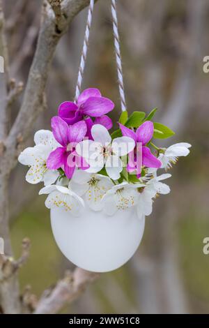 decorazione pasquale con fiori viola rosa e fiori di prato in un uovo appeso in giardino Foto Stock