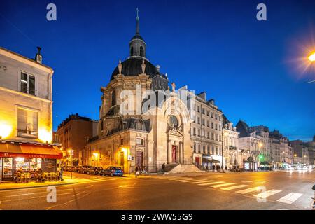 Il tramonto si adagia su Eglise Protestante du Marais con le luci della città che illuminano la strada. Foto Stock