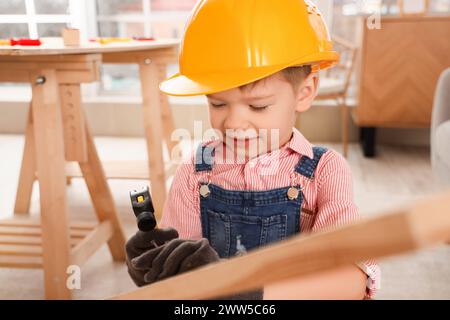 Un piccolo muratore che martellava un chiodo nella tavola di legno in camera, da vicino Foto Stock