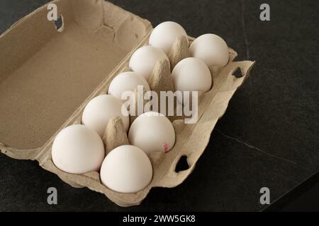 Mettere la scatola delle uova su un tavolo scuro con nove uova bianche. Manca un uovo nel mezzo. Foto Stock