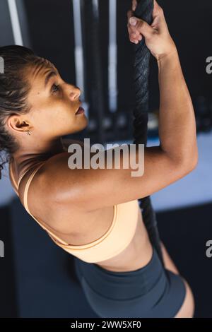 Una donna afroamericana in forma sta per scalare una corda in una palestra Foto Stock