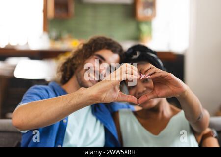 Una coppia diversificata forma il cuore con le mani a casa sul divano Foto Stock