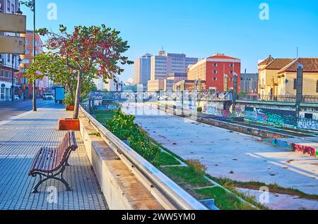 La passeggiata mattutina lungo l'essiccato fiume Guadalmedina con una vista sulle panchine e sugli alberi dell'Avenida de la Rosaleda e sul Ponte tedesco a dorso Foto Stock